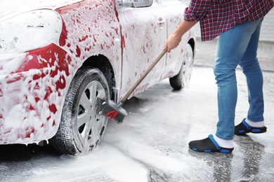 Photo of Young man cleaning vehicle with brush at self-service car wash