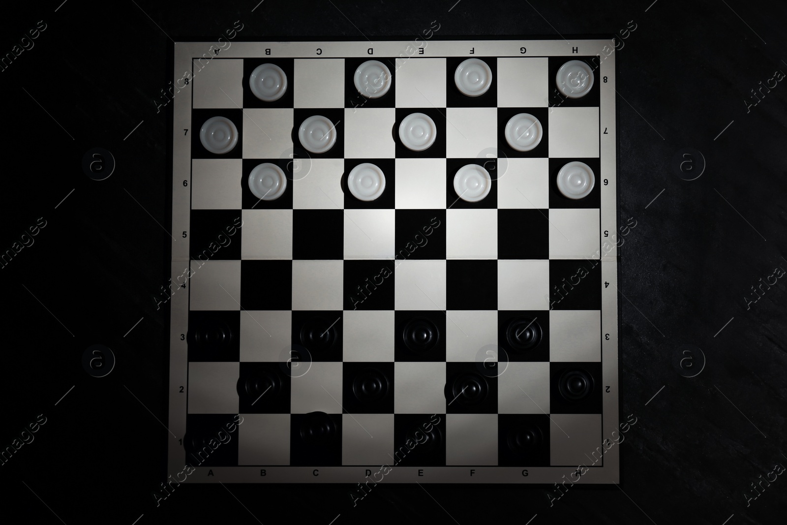 Photo of Checkerboard with game pieces on black table, top view