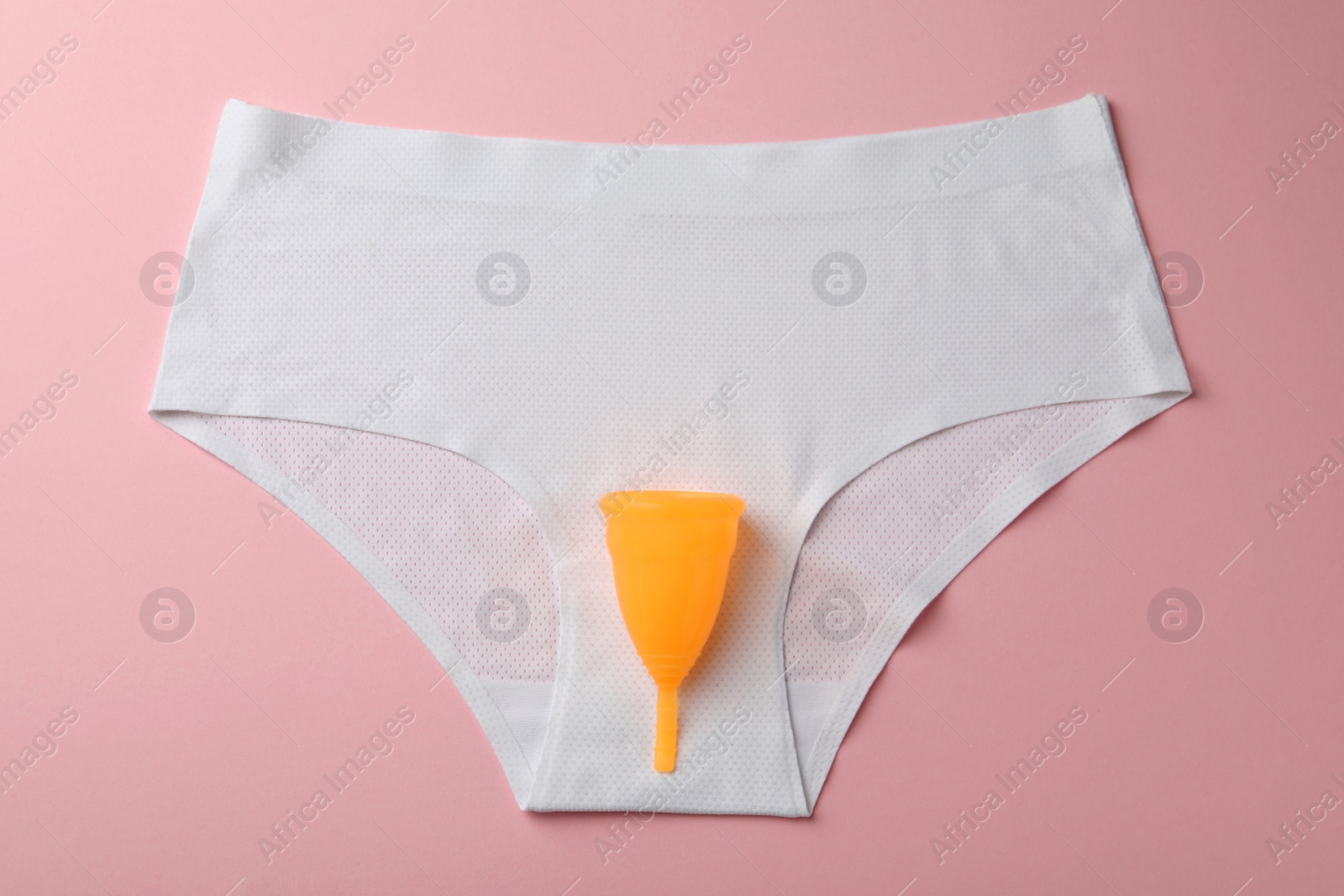 Photo of Menstrual cup and panties on pink background, top view