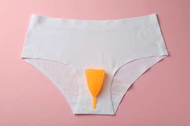 Menstrual cup and panties on pink background, top view