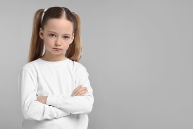Photo of Portrait of sad girl with crossed arms on light grey background, space for text