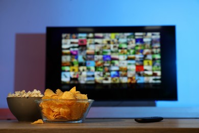 Photo of Bowls of snacks and TV remote control on table indoors