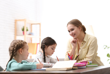 Photo of Mother helping her daughters with homework at table indoors