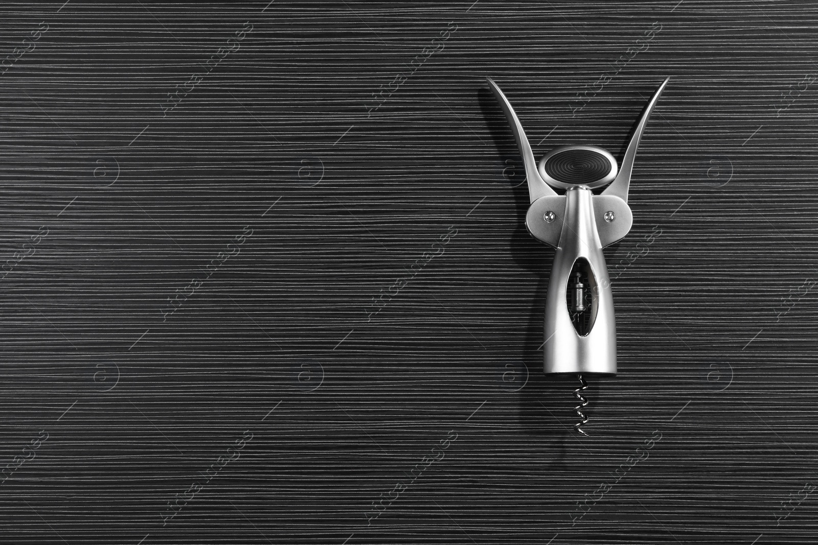 Photo of One wing corkscrew on black wooden table, top view. Space for text