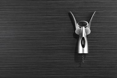 Photo of One wing corkscrew on black wooden table, top view. Space for text