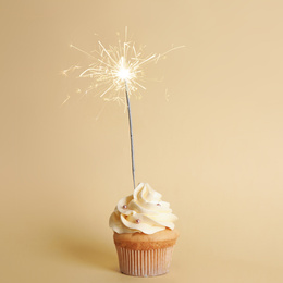 Birthday cupcake with sparkler on beige background