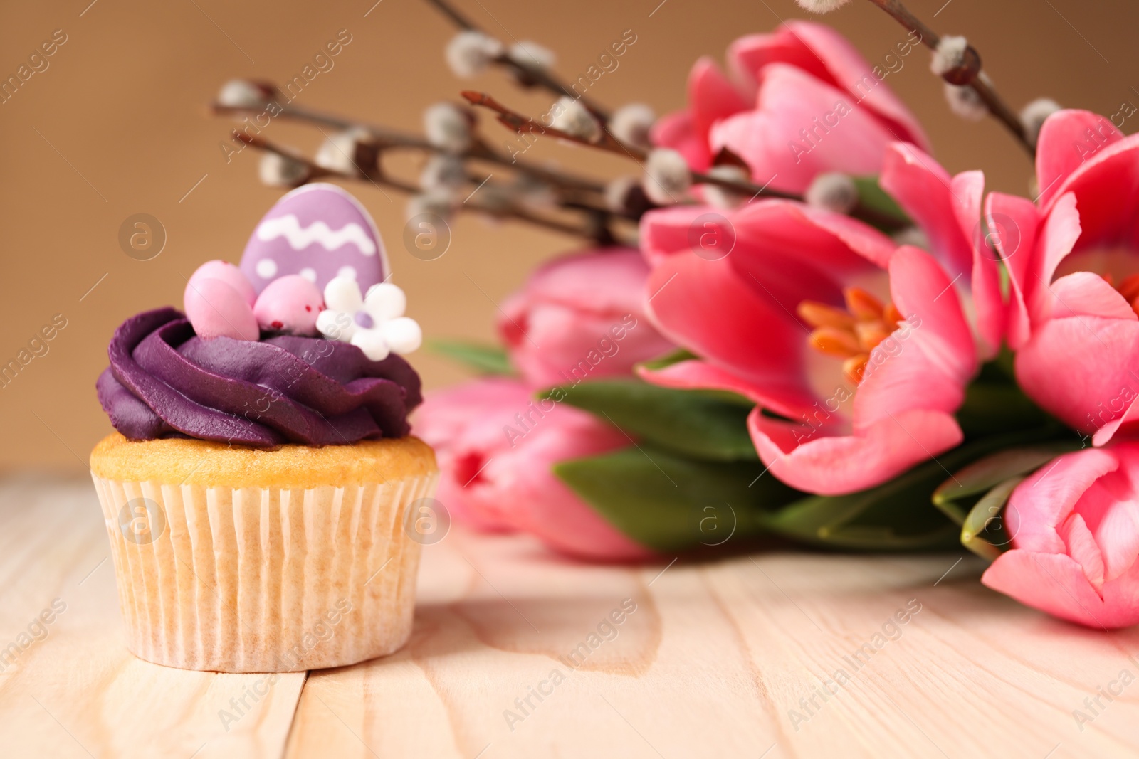 Photo of Tasty decorated Easter cupcake, flowers and willow branches on wooden table