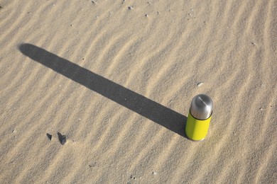 Photo of Yellow thermos with hot drink on sand, above view. Space for text