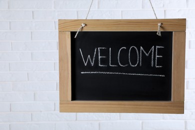Photo of Small chalkboard with word Welcome hanging near white brick wall. Space for text