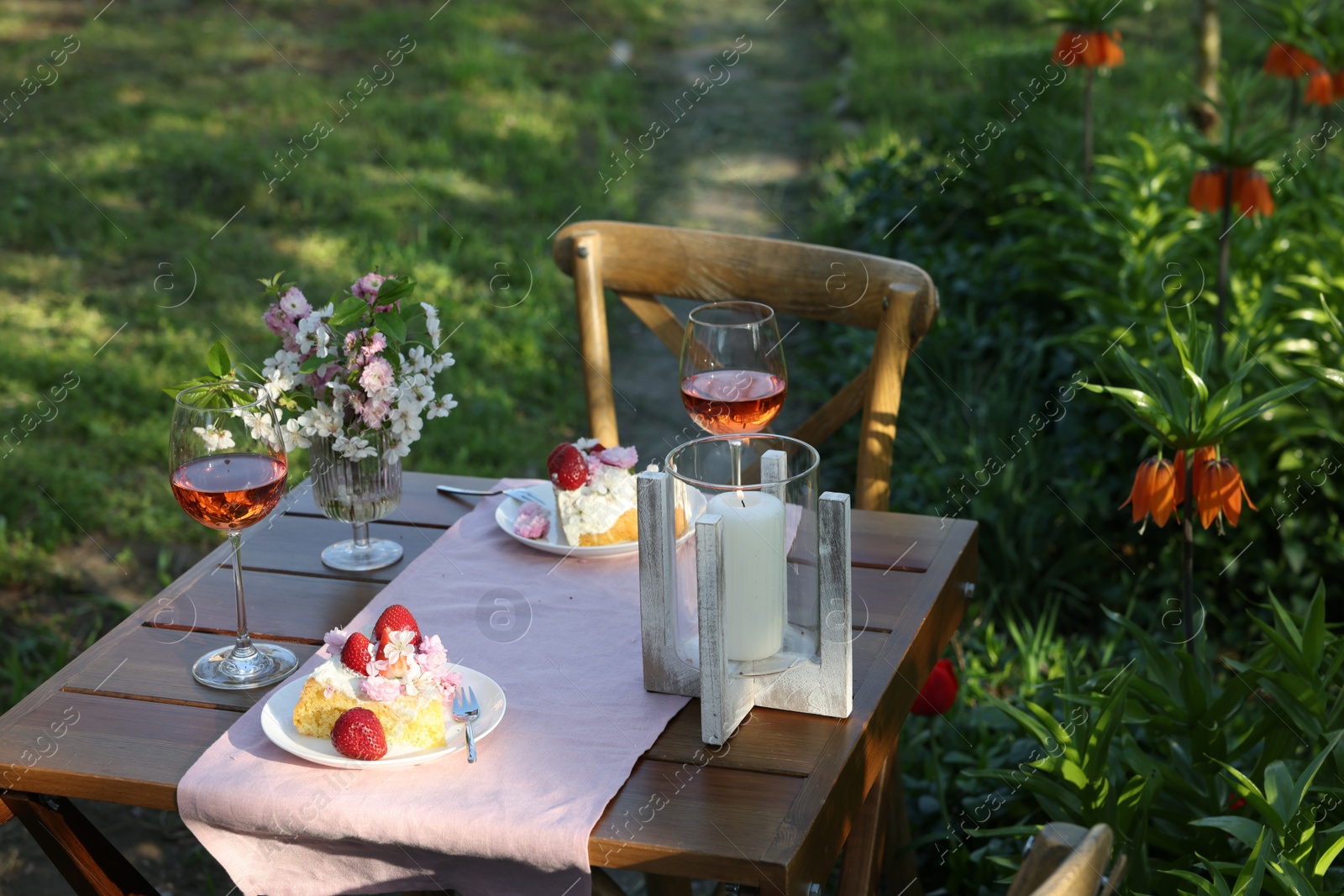 Photo of Vase with spring flowers, wine and cake on table served for romantic date in garden