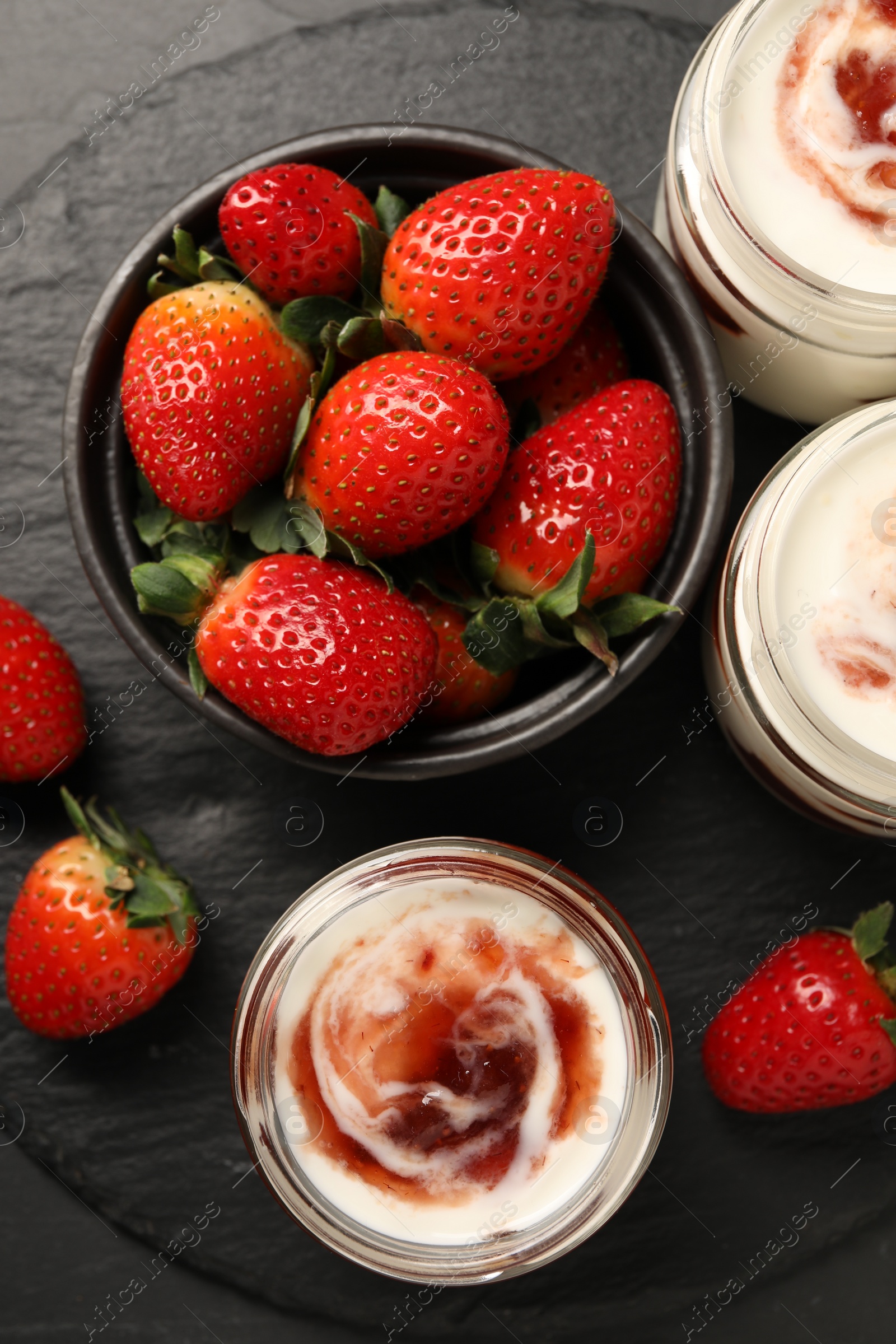 Photo of Tasty yoghurt with jam and strawberries on black table, top view