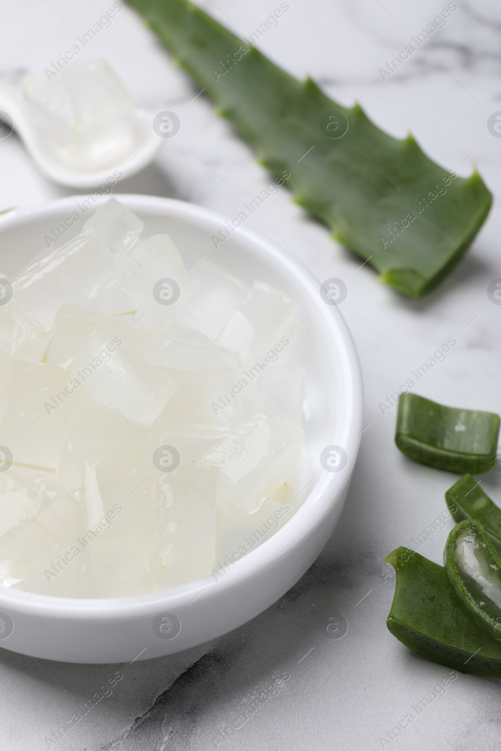 Photo of Aloe vera gel and slices of plant on white marble table, closeup