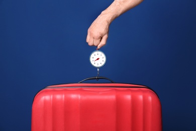Man weighing stylish suitcase against color background, closeup