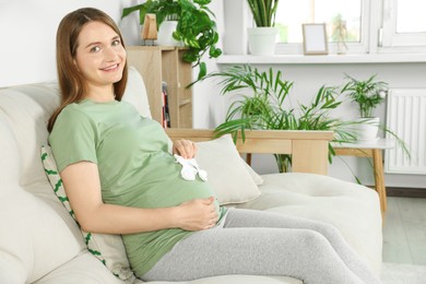 Photo of Pregnant woman sitting on sofa with baby socks in living room