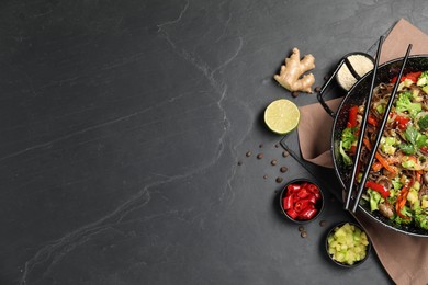 Wok with noodles, mushrooms, vegetables and other products on black table, flat lay. Space for text