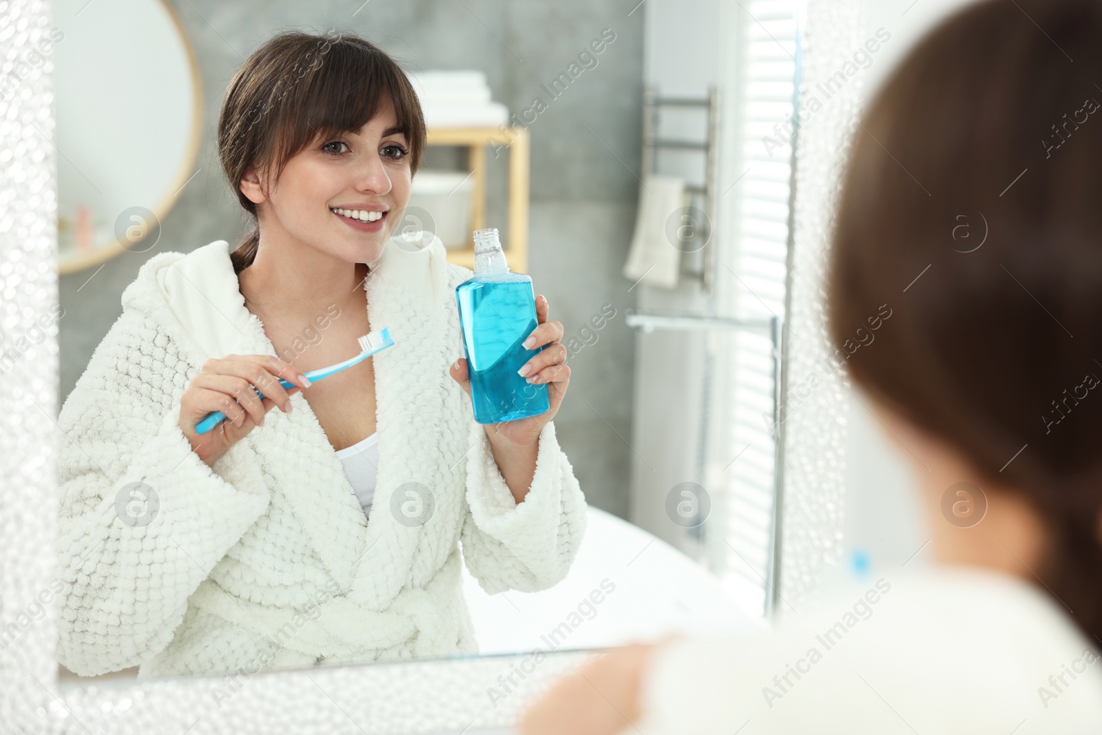 Photo of Young woman using mouthwash near mirror in bathroom