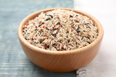 Photo of Mix of different brown rice in bowl on light blue wooden table