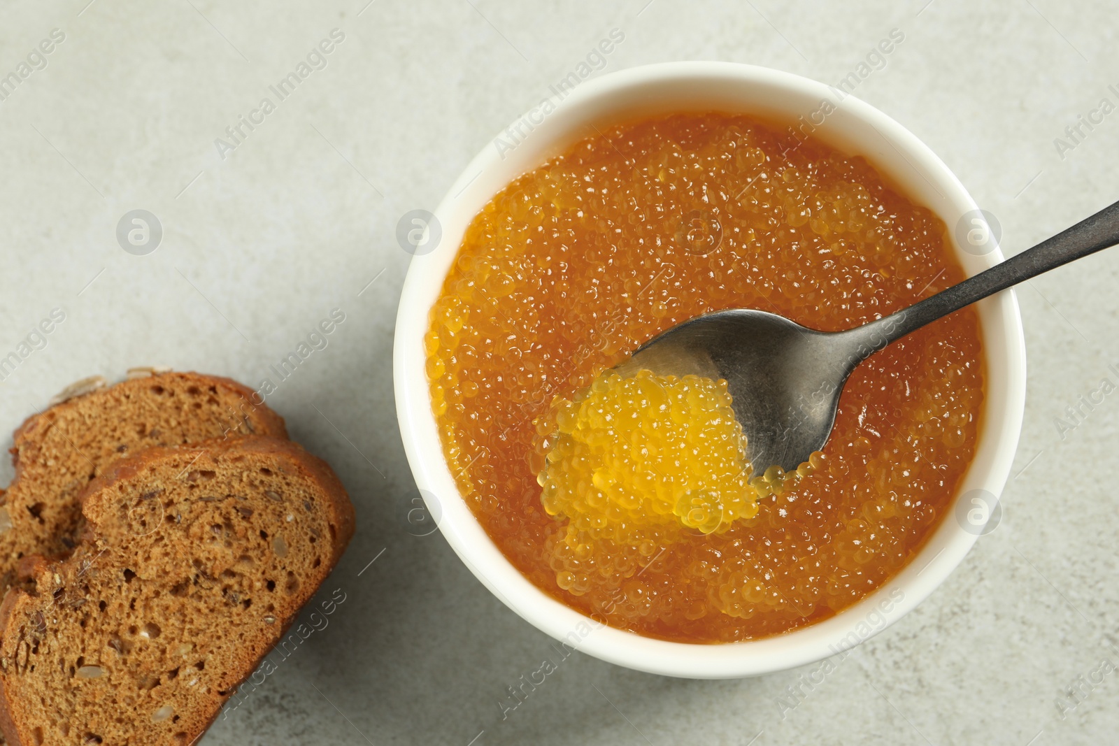 Photo of Fresh pike caviar in bowl, spoon and bread on light grey table, top view