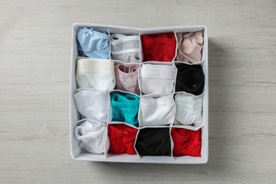 Photo of Organizer with folded women's underwear on light wooden table, top view