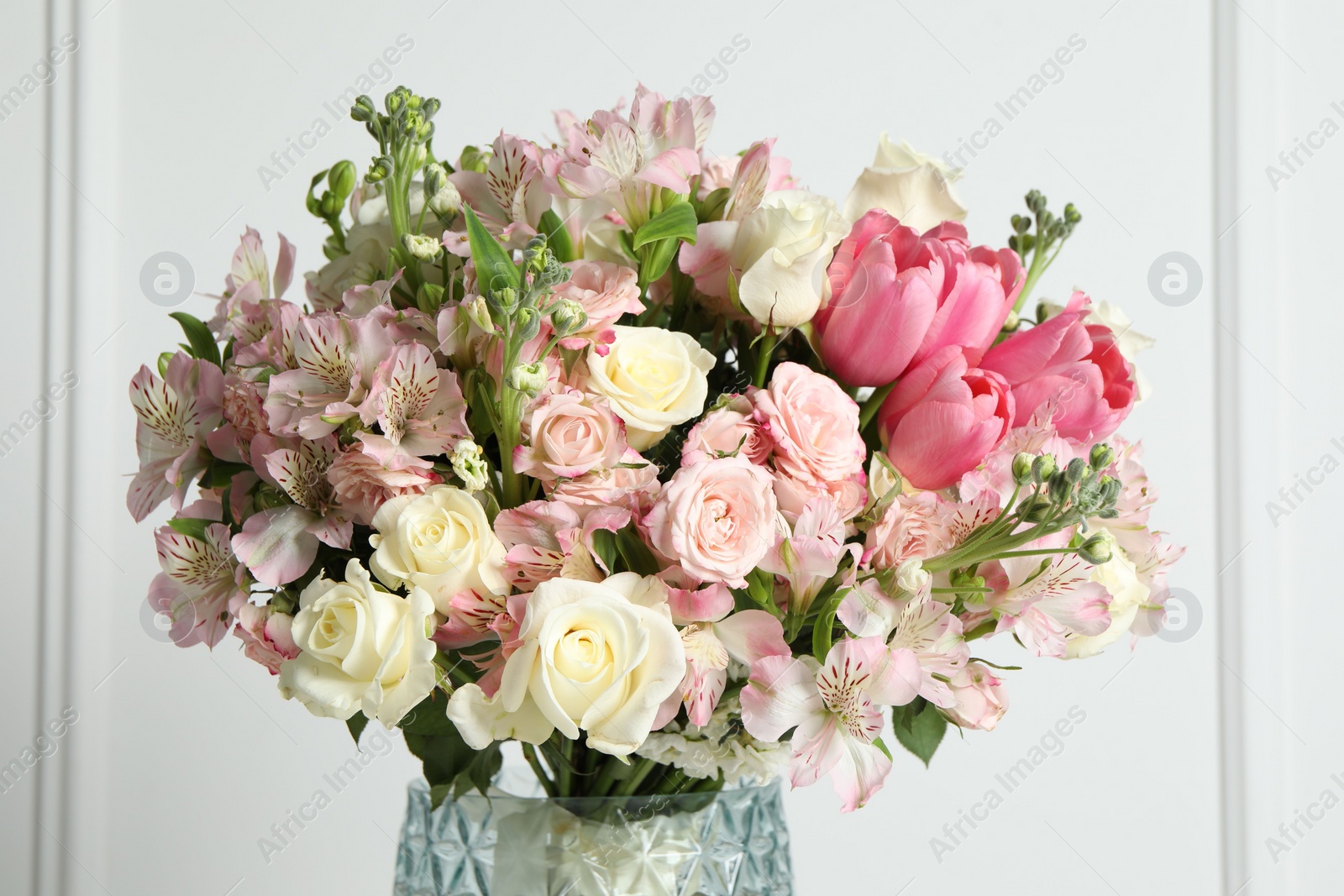 Photo of Beautiful bouquet of fresh flowers in vase near white wall