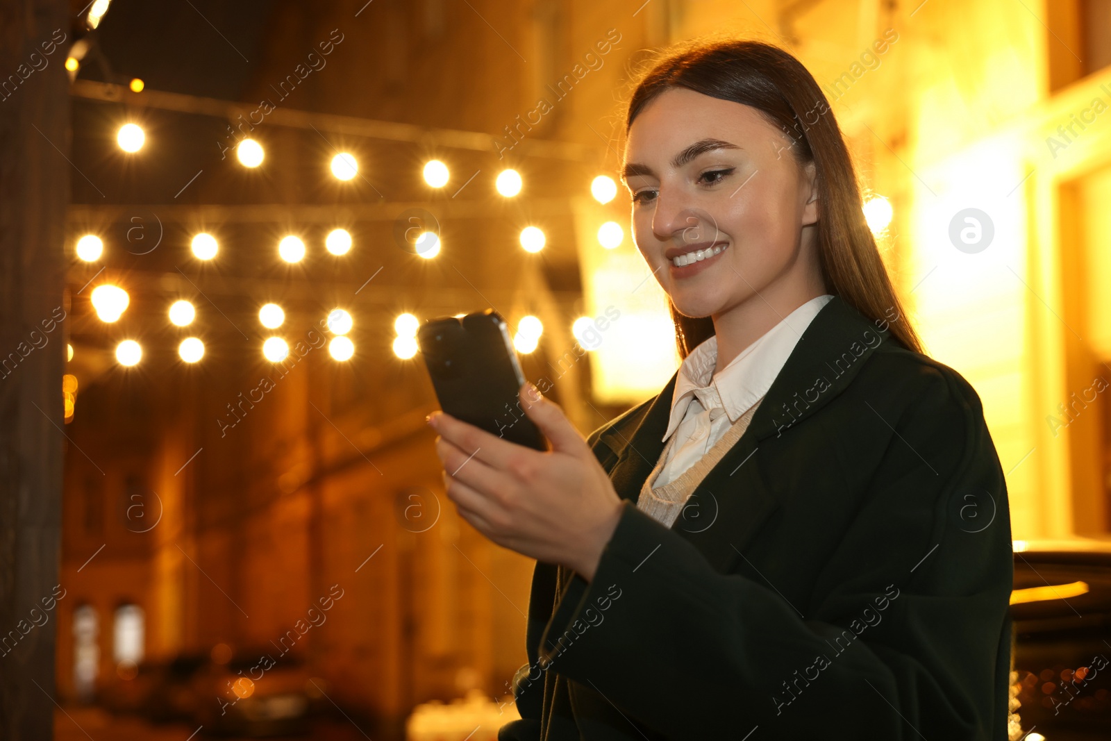 Photo of Smiling woman using smartphone on night city street. Space for text