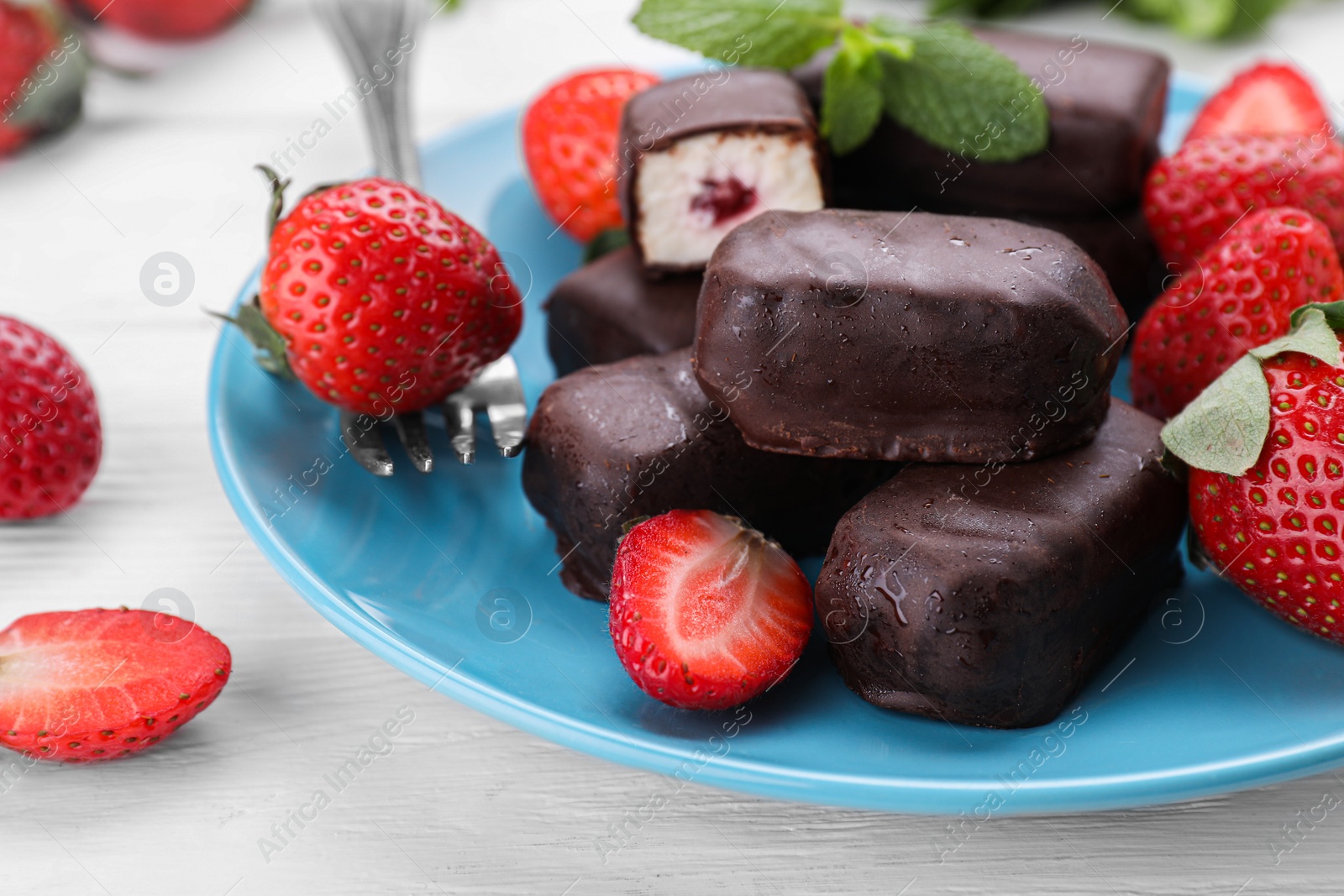 Photo of Delicious glazed curd snacks and fresh strawberries on white wooden table, closeup