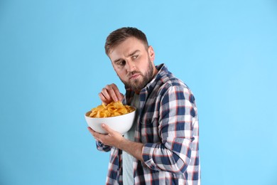 Photo of Greedy young man hiding bowl with chips on light blue background
