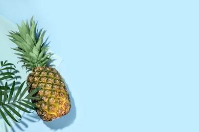Whole ripe pineapple and green leaves on light blue background, flat lay. Space for text