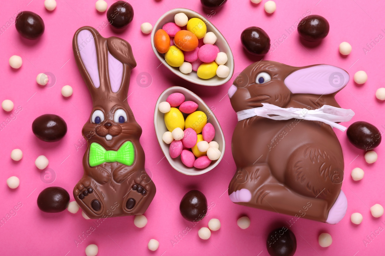 Photo of Chocolate Easter bunnies, halves of egg and candies on pink background, flat lay