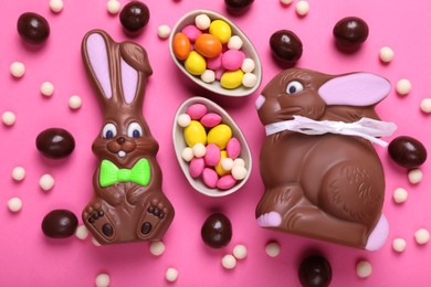 Chocolate Easter bunnies, halves of egg and candies on pink background, flat lay