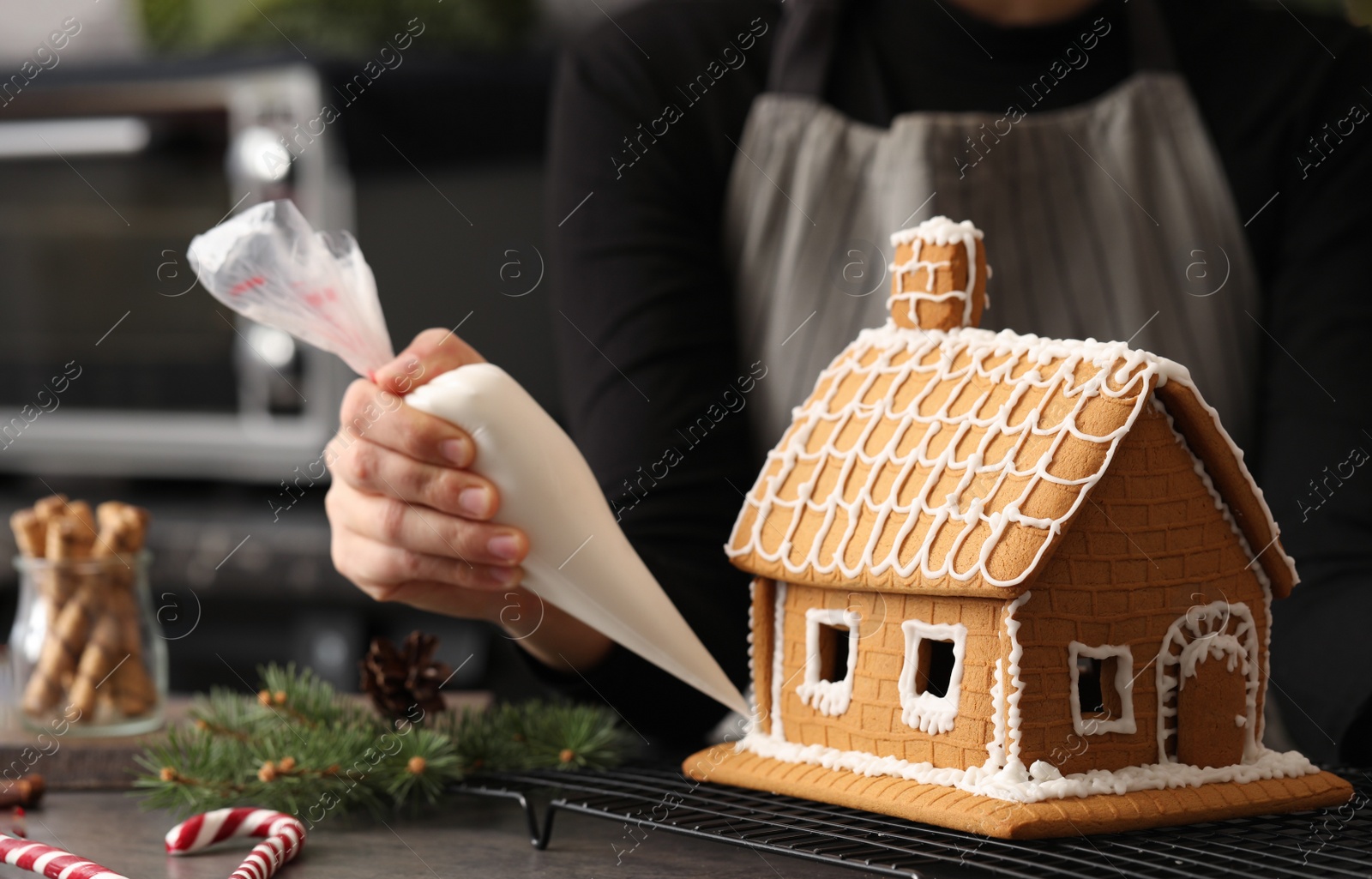 Photo of Woman decorating gingerbread house with icing at grey table, closeup