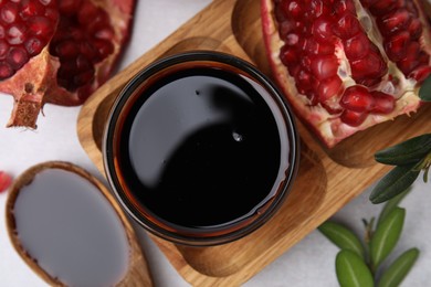 Photo of Tasty pomegranate sauce, fruits and branches on white table, flat lay