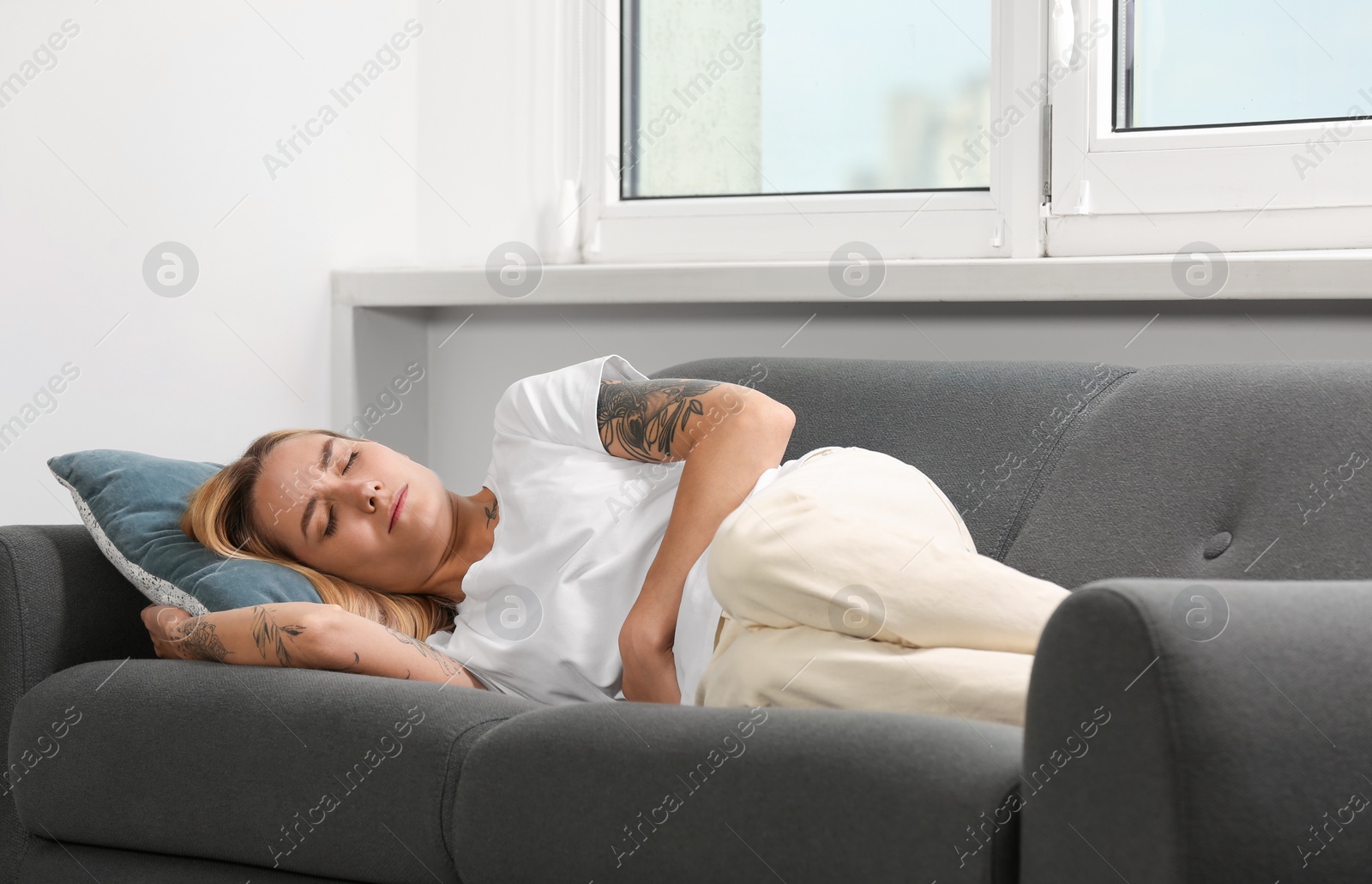 Photo of Young woman suffering from menstrual pain on sofa indoors