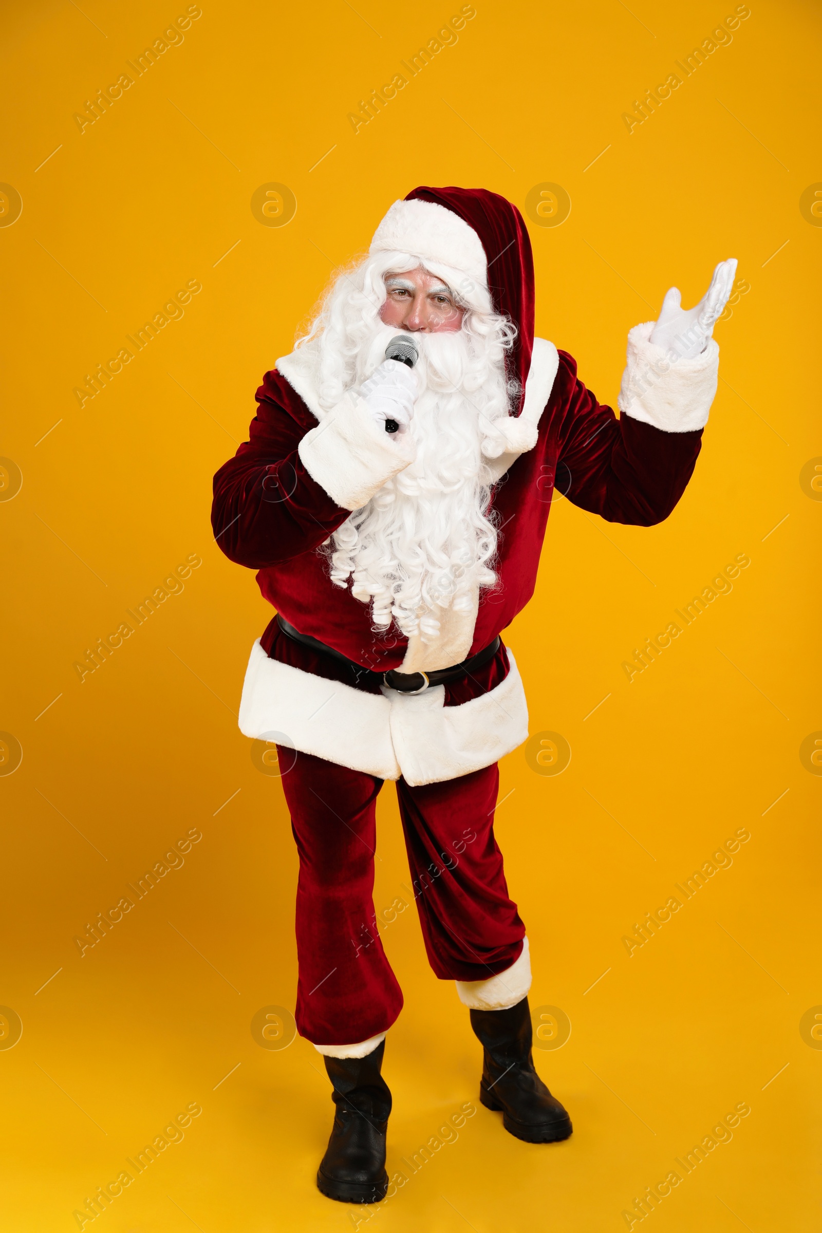 Photo of Santa Claus singing with microphone on yellow background. Christmas music