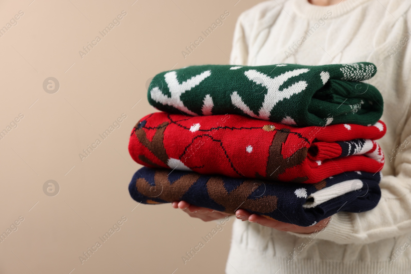 Photo of Woman holding stack of different Christmas sweaters on beige background, closeup. Space for text