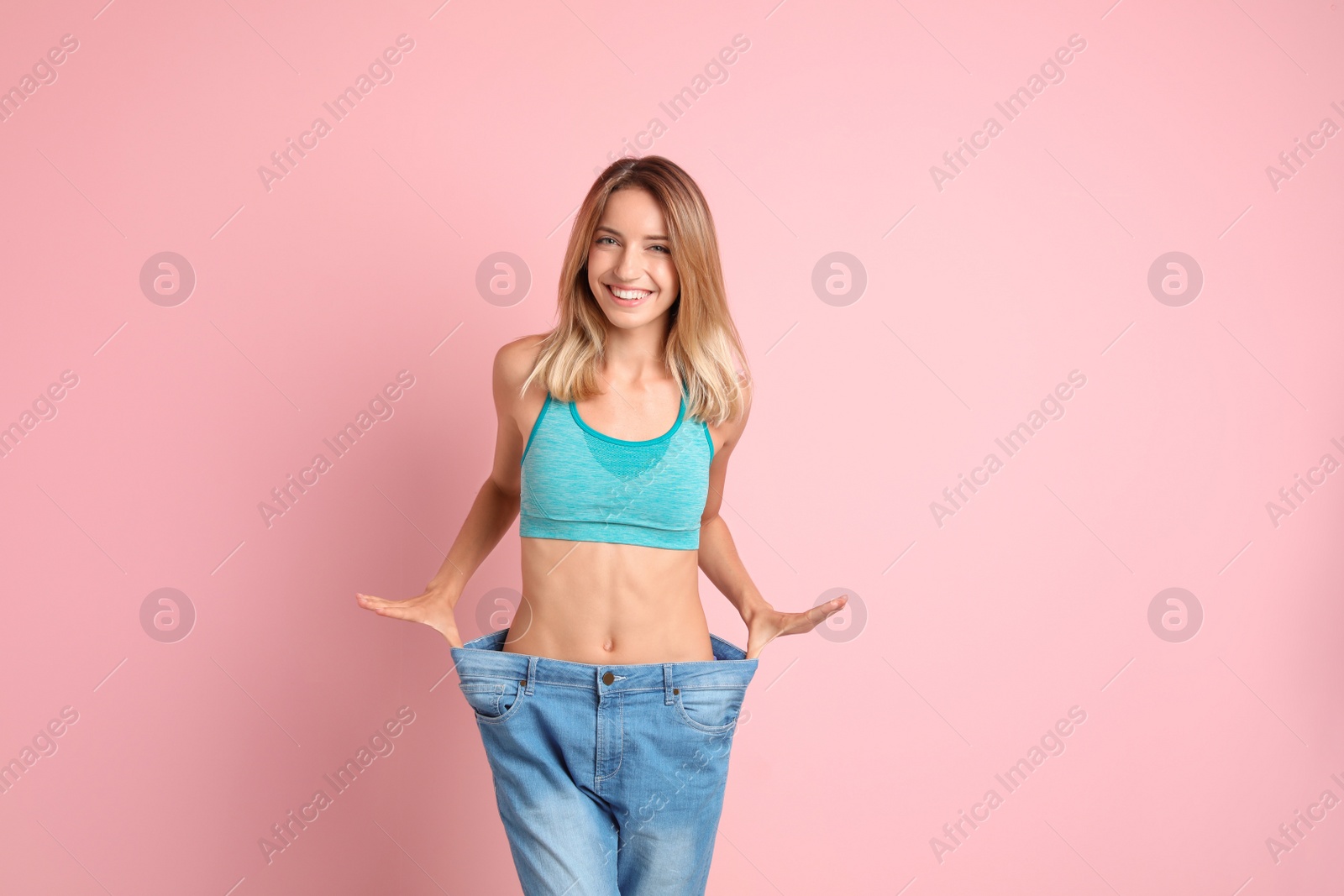 Photo of Young slim woman in old big jeans showing her diet results on color background