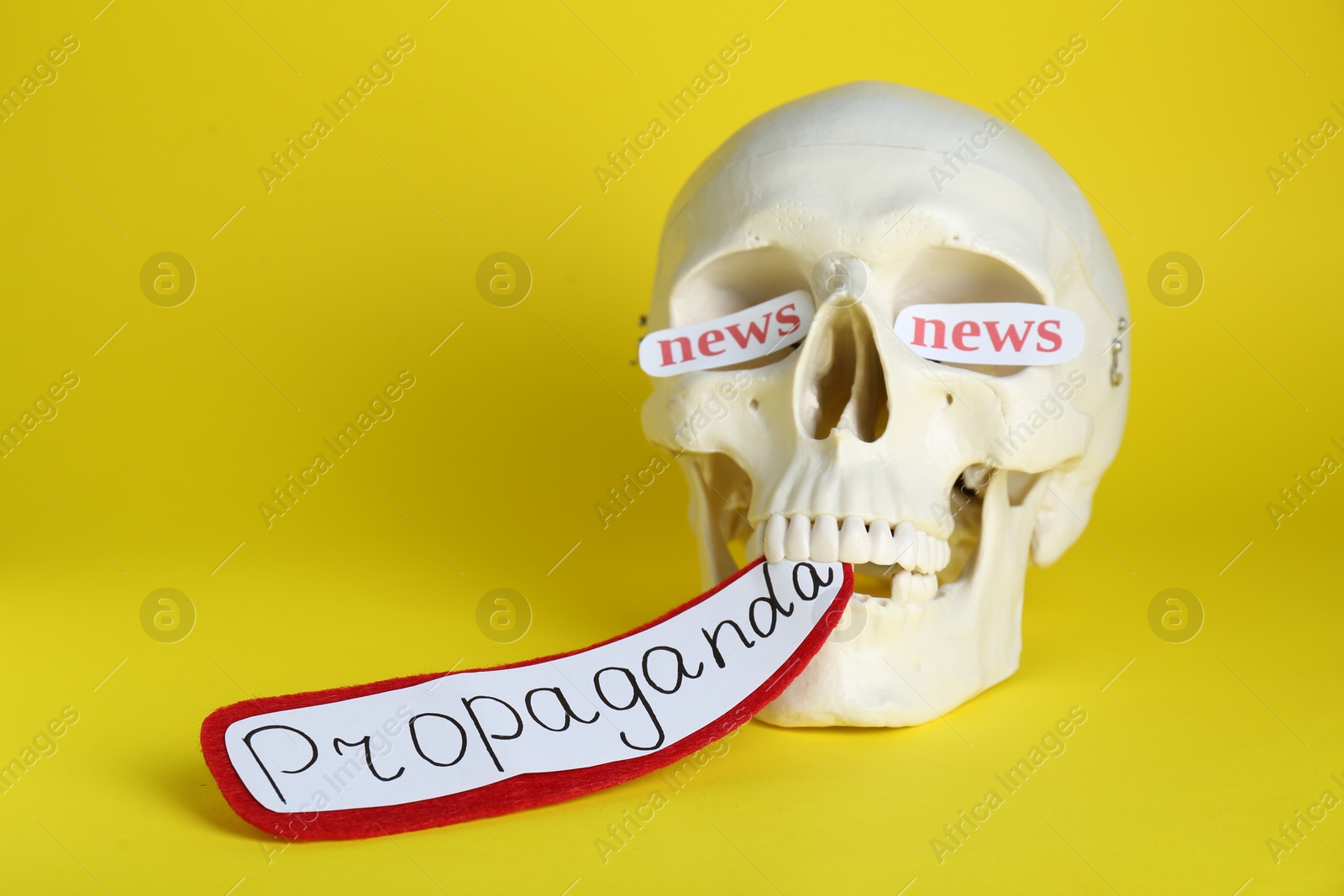 Photo of Information warfare concept. Paper cards with words news in eye sockets of human skull and text Propaganda in teeth on yellow background