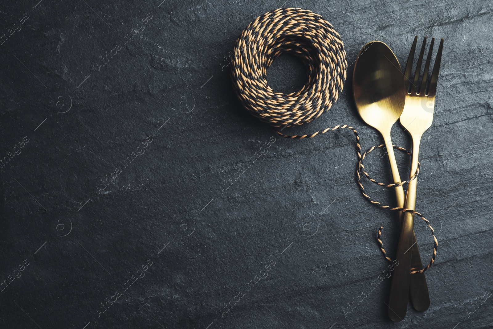 Photo of Cutlery and rope on black slate background, flat lay with space for text. Table setting elements