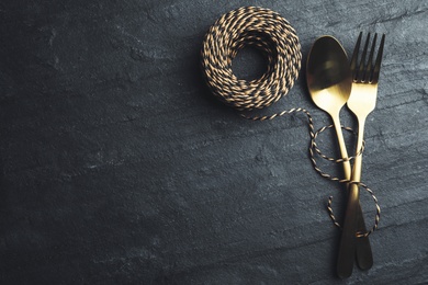 Cutlery and rope on black slate background, flat lay with space for text. Table setting elements