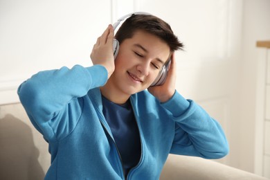 Photo of Cute teenage boy with headphones listening music on sofa at home