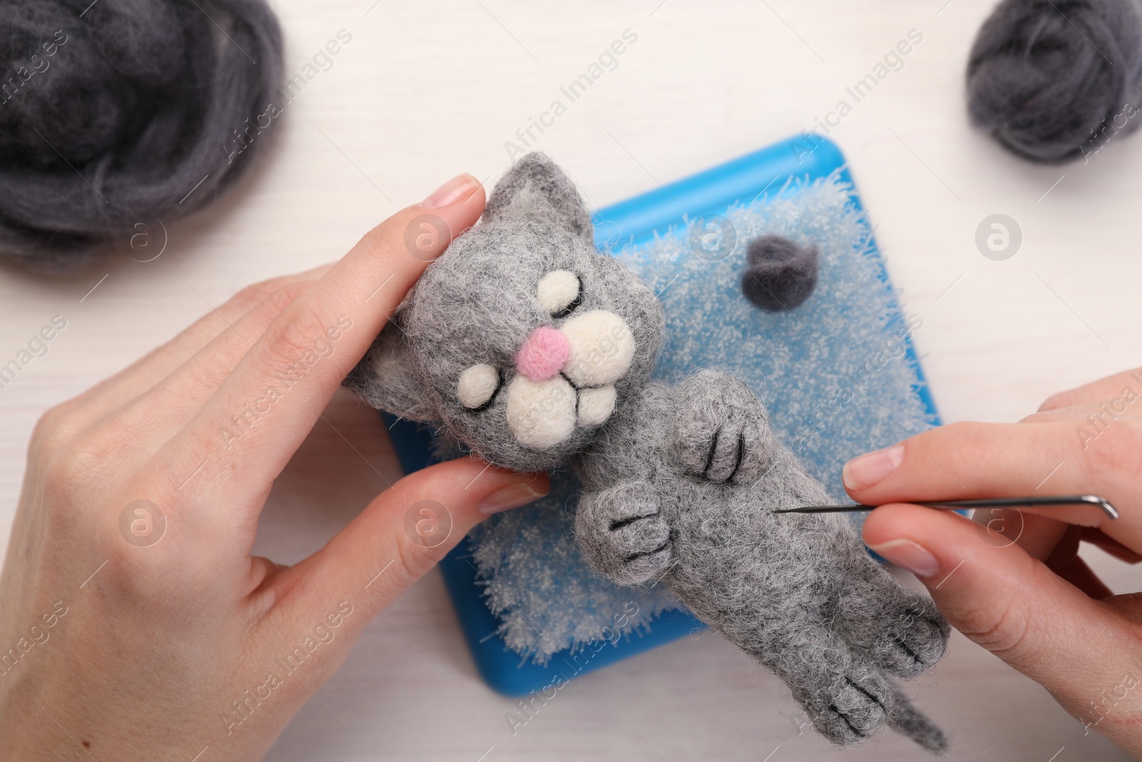Photo of Woman felting toy cat from wool at light wooden table, top view