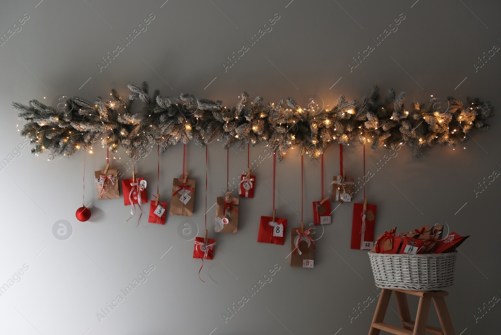 Photo of Christmas advent calendar with decorative fir branches and fairy lights hanging on wall