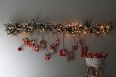 Photo of Christmas advent calendar with decorative fir branches and fairy lights hanging on wall