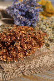 Photo of Different dry herbs and burlap fabric on table, closeup