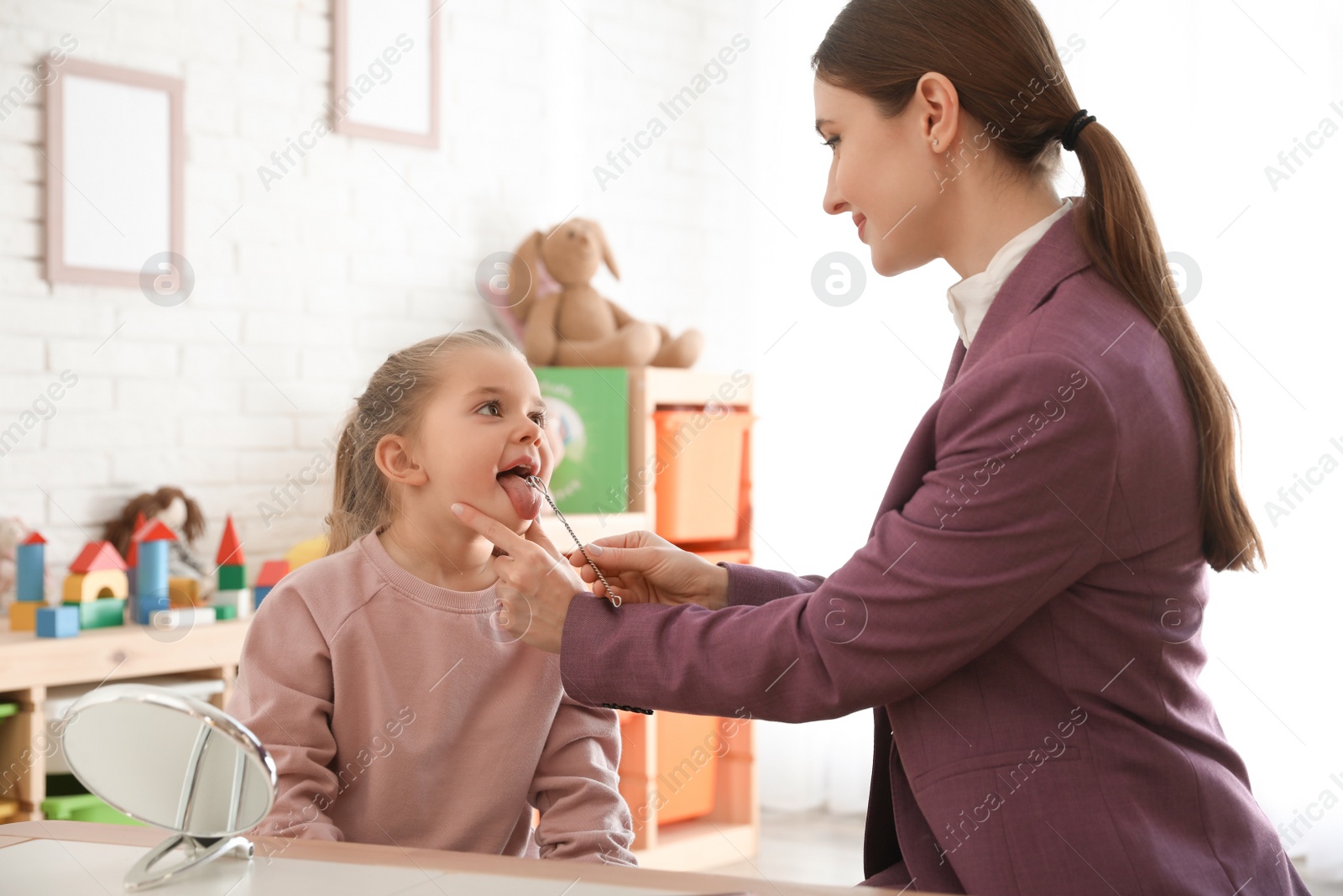 Photo of Speech therapist using logopedic probe on session with little girl in office