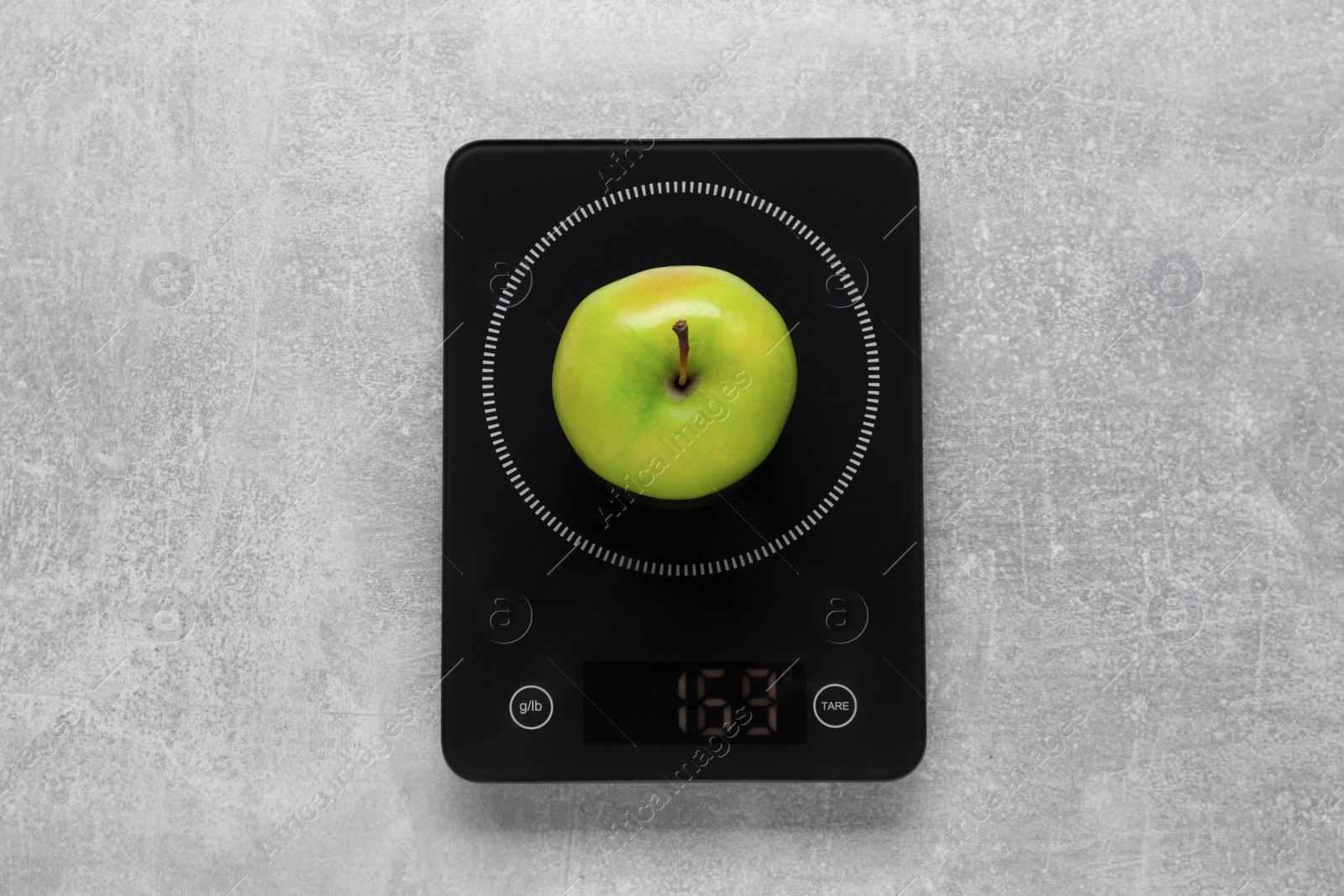 Photo of Digital kitchen scale with ripe green apple on grey table, top view