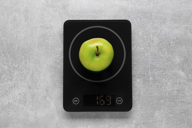 Photo of Digital kitchen scale with ripe green apple on grey table, top view
