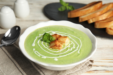 Photo of Delicious broccoli cream soup with croutons served on white wooden table
