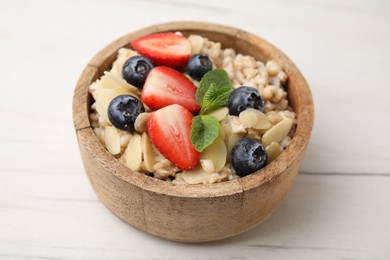 Photo of Tasty oatmeal with strawberries, blueberries and almond petals in bowl on white wooden table, closeup