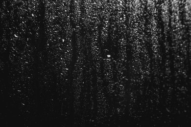 Photo of Glass with rain drops on black background